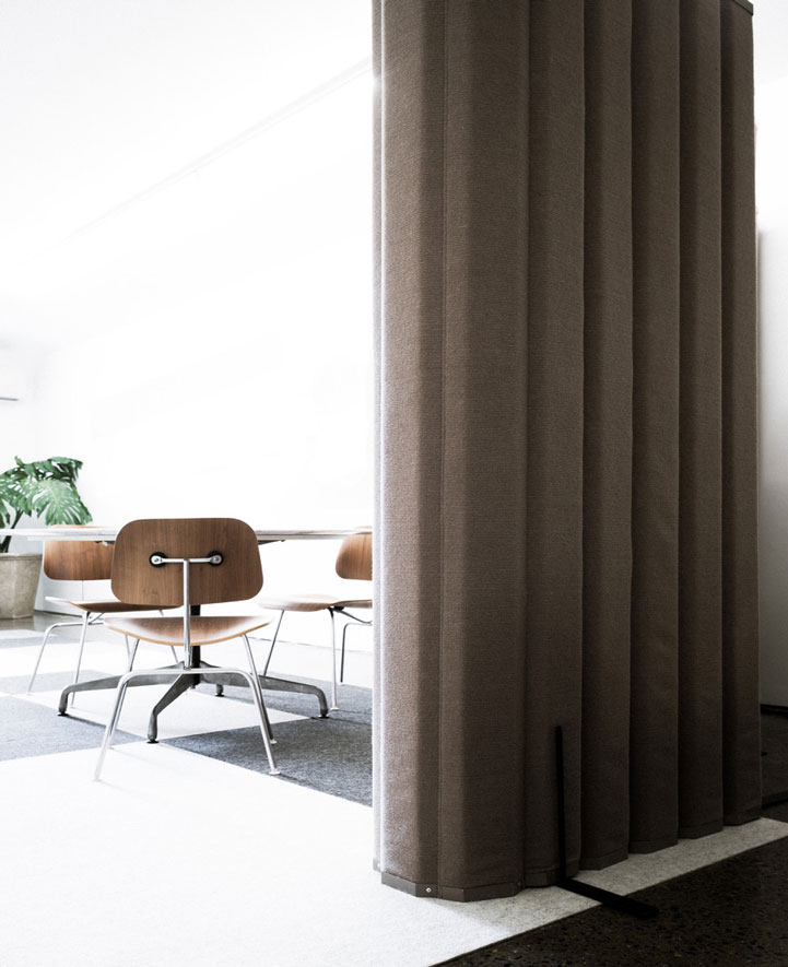 The VersiPanel Acoustical Wall Partition is folded up near a table in a business space.