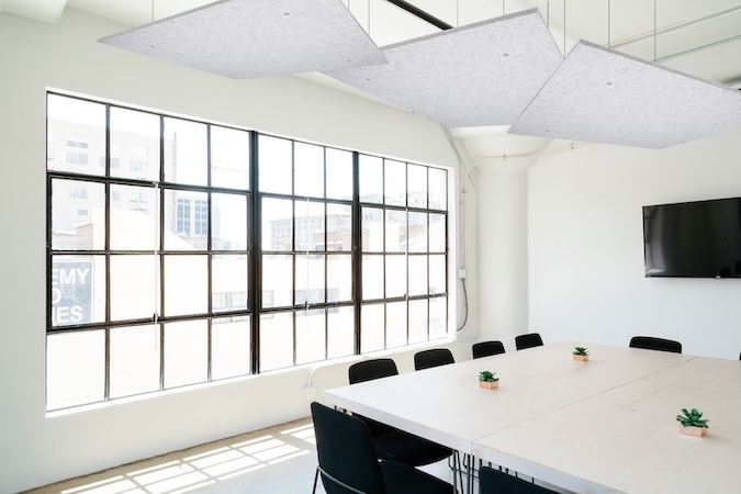 Light gray SoundSorb acoustic ceiling canopies suspended above a modern conference table in a bright meeting room with large windows.