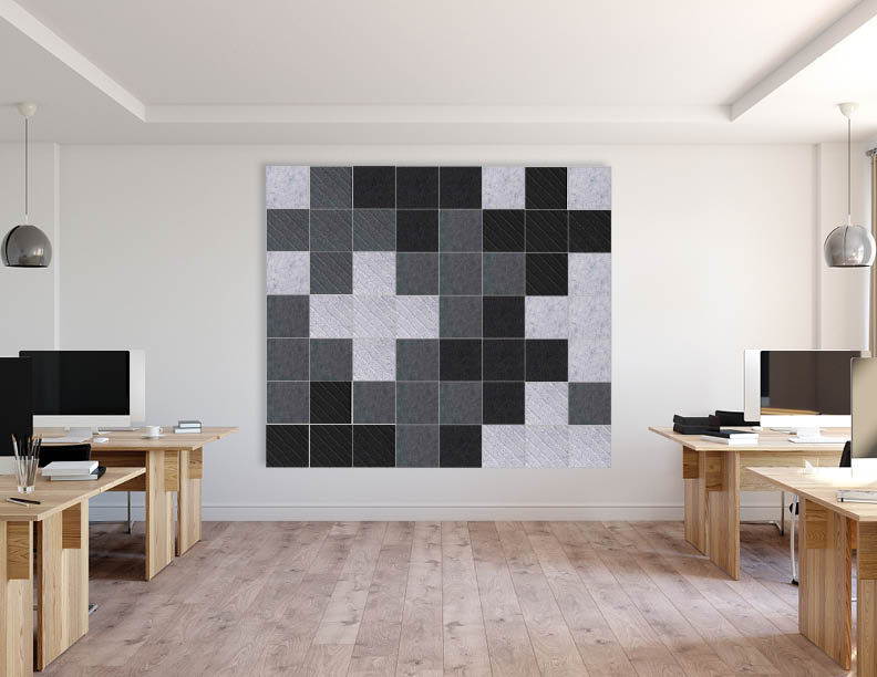 Modern open office with wooden desks and computer monitors, featuring a large geometric arrangement of gray, black, and white rectangular acoustic wall panels.