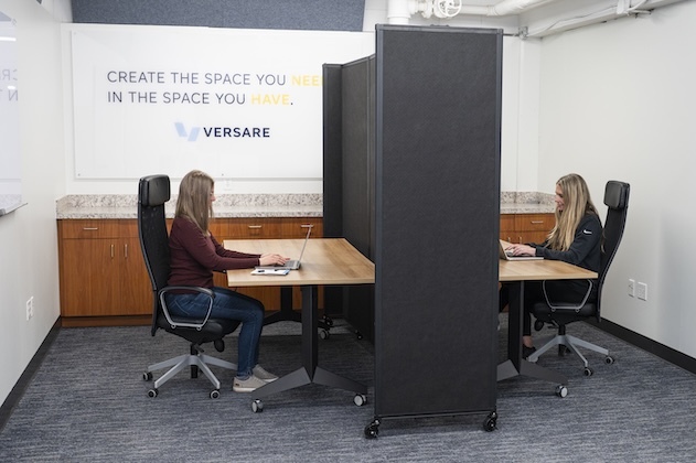Two women working at separate desks divided by a portable Room Divider 360&reg; office partition