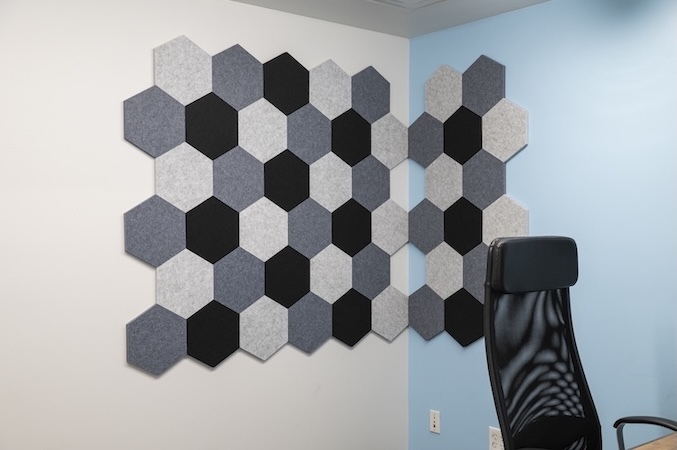 Office with gray, white, and black hexagon acoustic wall tiles in a geometric pattern.