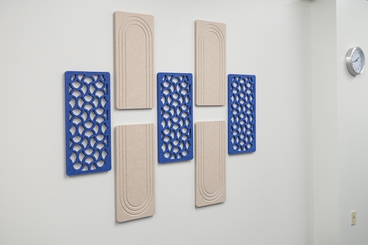 Decorative acoustic wall installation featuring alternating blue patterned panels and tall beige textured panels arranged on a white wall.