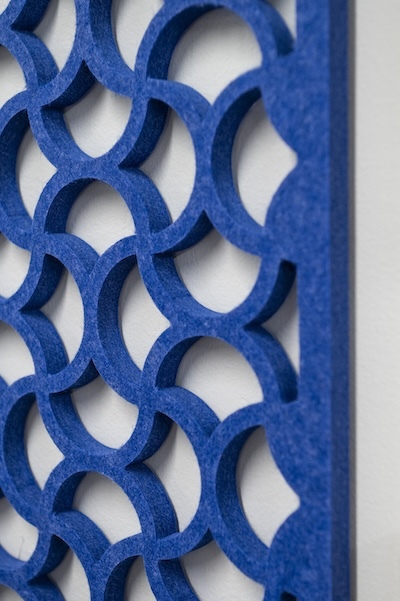 Close-up angled view of a blue decorative acoustic wall panel featuring an interlocking circular geometric pattern with a textured finish, mounted against a white wall.