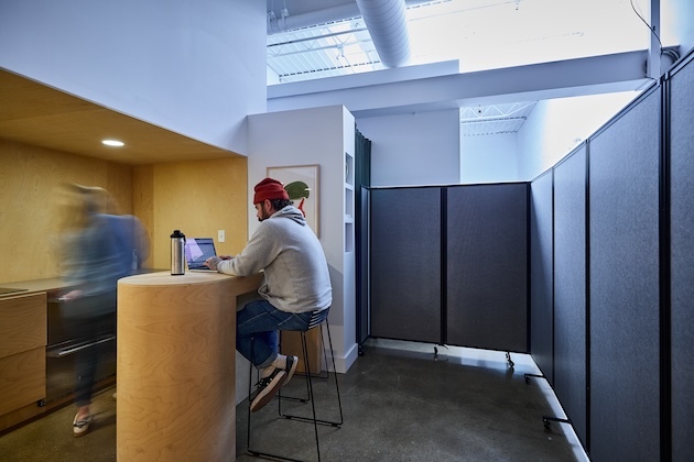 Dark gray room divider arranged in an L-shape configuration to create a private workspace beside a counter.