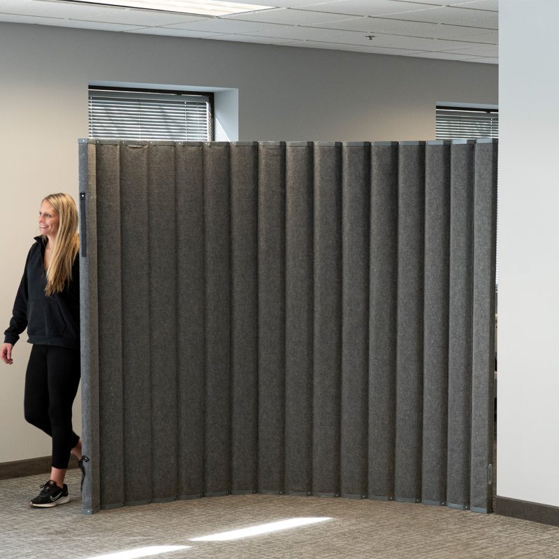 Folding gray fabric accordion partition used as a movable room divider in an office space.