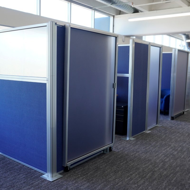 Blue fabric office cubicles with aluminum frames and a frosted sliding door in a modern workspace.