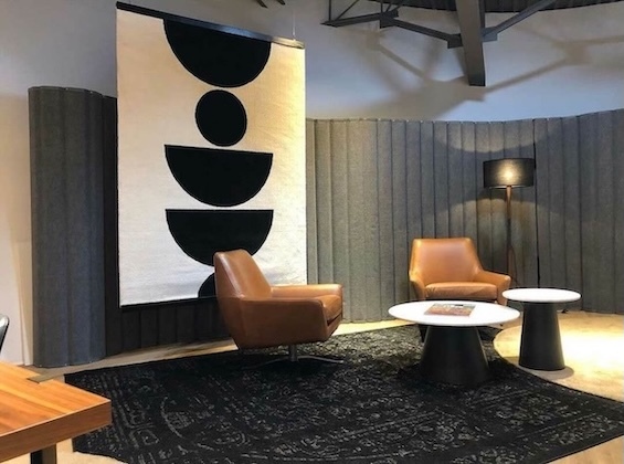 Modern lounge with gray acoustic wall panels, leather chairs, round tables, and abstract wall art.